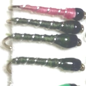 Può includere: Assortimento di materiali per legare mosche, tra cui una varietà di colori di filo per legare mosche e perline nere. Il filo è avvolto attorno a un amo.