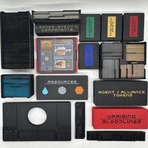 Puede incluir: Una colección de componentes de juegos de mesa, incluyendo cajas con las etiquetas "PLAYER COMPONENTS" y "LEADER-SPECIFIC COMPONENTS". La imagen presenta varios contenedores, fichas de recursos y un tablero de juego con imágenes desérticas. El texto "UPRISING BLOODLINES" es visible.
