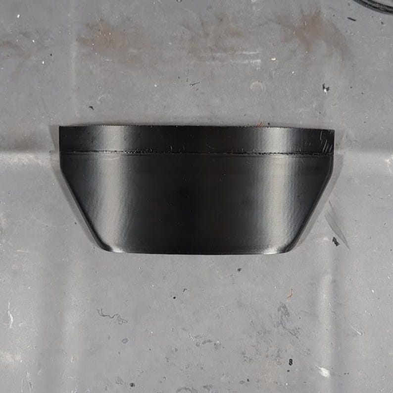 May include: A black, trapezoidal-shaped object with a smooth, reflective surface. The object has a slightly curved top edge and angled sides, giving it a modern, minimalist appearance. The object appears to be made of a solid material.