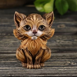 Pu&ograve; includere: Una piccola statuetta di legno intagliata in modo intricato di un gatto marrone e bianco con grandi occhi. Il gatto &egrave; seduto con le zampe ripiegate sotto di lui.