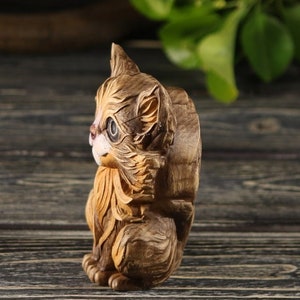 Pu&ograve; includere: Una statuetta di legno intagliata a mano di un gatto marrone e bianco seduto con la testa girata di lato. Il gatto ha un viso dettagliato con occhi dipinti e una coda folta.