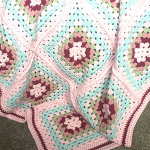 May include: A pink, green and red crochet blanket with a granny square pattern.