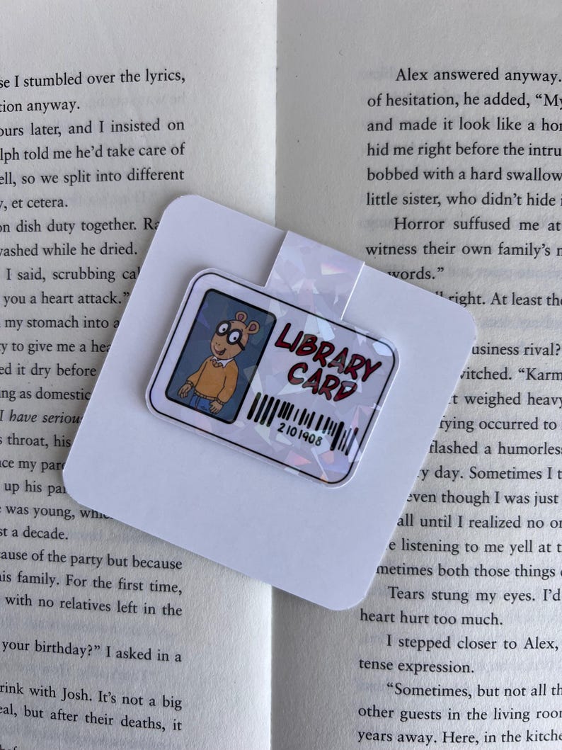 Puede incluir: Un marcap&aacute;ginas colorido con un personaje de dibujos animados del programa infantil "Arthur." El marcap&aacute;ginas tiene un acabado hologr&aacute;fico y dice "Library Card" con un c&oacute;digo de barras que dice "2101408."