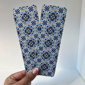 Peut inclure: Deux marque-pages décoratifs avec un motif floral de carreaux bleus, blancs et dorés. Les marque-pages sont maintenus, mettant en valeur le motif complexe. Le motif rappelle les carreaux traditionnels, ajoutant une touche d'élégance.