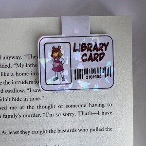 Puede incluir: Una tarjeta de biblioteca rosa y blanca con un c&oacute;digo de barras y el texto "LIBRARY CARD" en negro. Una imagen de dibujos animados de una ni&ntilde;a con cabello casta&ntilde;o y un vestido rosa est&aacute; en la esquina superior izquierda.