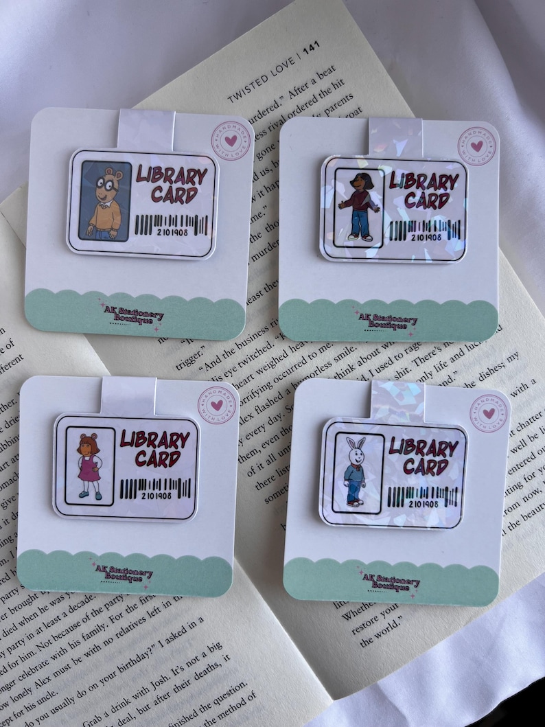 Puede incluir: Cuatro imanes de marcadores hologr&aacute;ficos de colores con personajes de la serie de televisi&oacute;n animada Arthur. Cada marcador presenta un rect&aacute;ngulo blanco con el texto "Library Card" y un c&oacute;digo de barras con el n&uacute;mero "2101908".