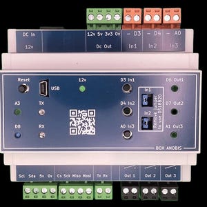 Könnte beinhalten: Ein rechteckiges elektronisches Gerät mit einer blau-weißen Frontplatte. Es verfügt über verschiedene Anschlüsse, darunter USB, und beschriftete Klemmen für Strom- und Datenverbindungen. Das Gerät hat einen QR-Code und den Text "BOX ANOBIS".