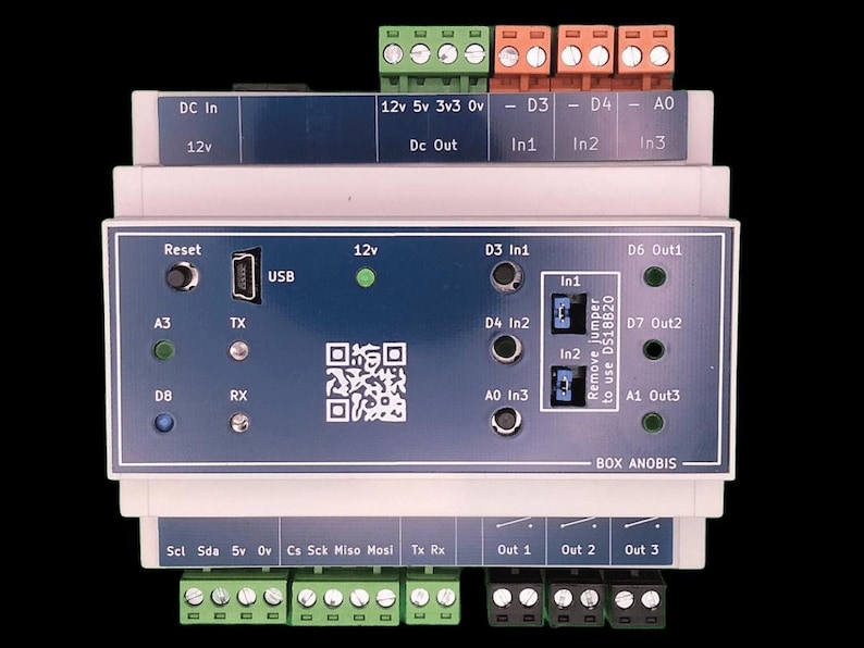 May include: A rectangular electronic device with a blue and white faceplate. It features various ports, including USB, and labeled terminals for power and data connections. The device has a QR code and the text "BOX ANOBIS".