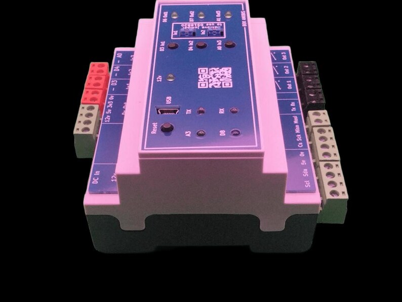 May include: A pink and blue electronic circuit board with various ports, connectors, and a USB port. The board has text and a QR code printed on it. The device has red, black, and green connectors on the sides.