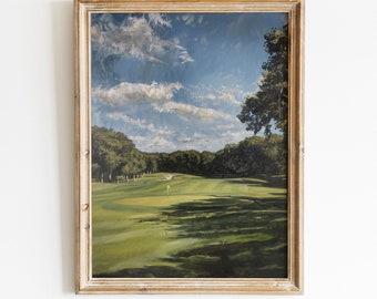 May include: A framed landscape painting of a golf course under a blue sky with fluffy white clouds. The artwork features a green fairway, trees, and a flag on the green. The frame is a light, warm color. The text "OUT WANDERING Design" is at the bottom.