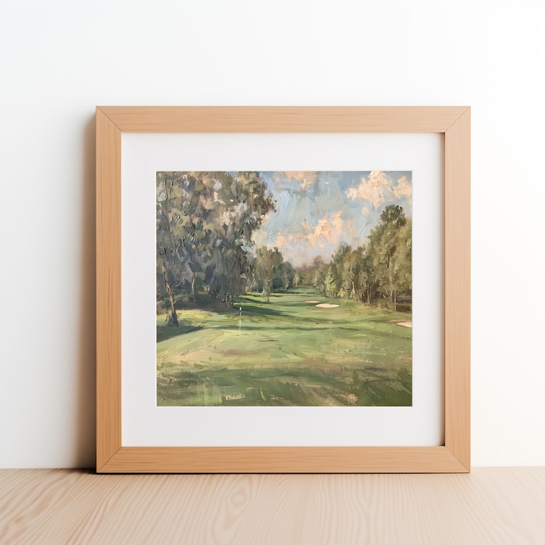 May include: A framed painting of a golf course with green grass, trees, and a blue sky with white clouds. The painting is in a light wood frame.