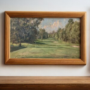 May include: A framed oil painting depicting a golf course with green grass, trees, and a blue sky with white clouds. The painting is in a wooden frame.