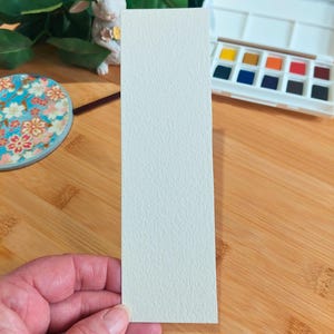 May include: A white watercolor paper bookmark with a textured surface.