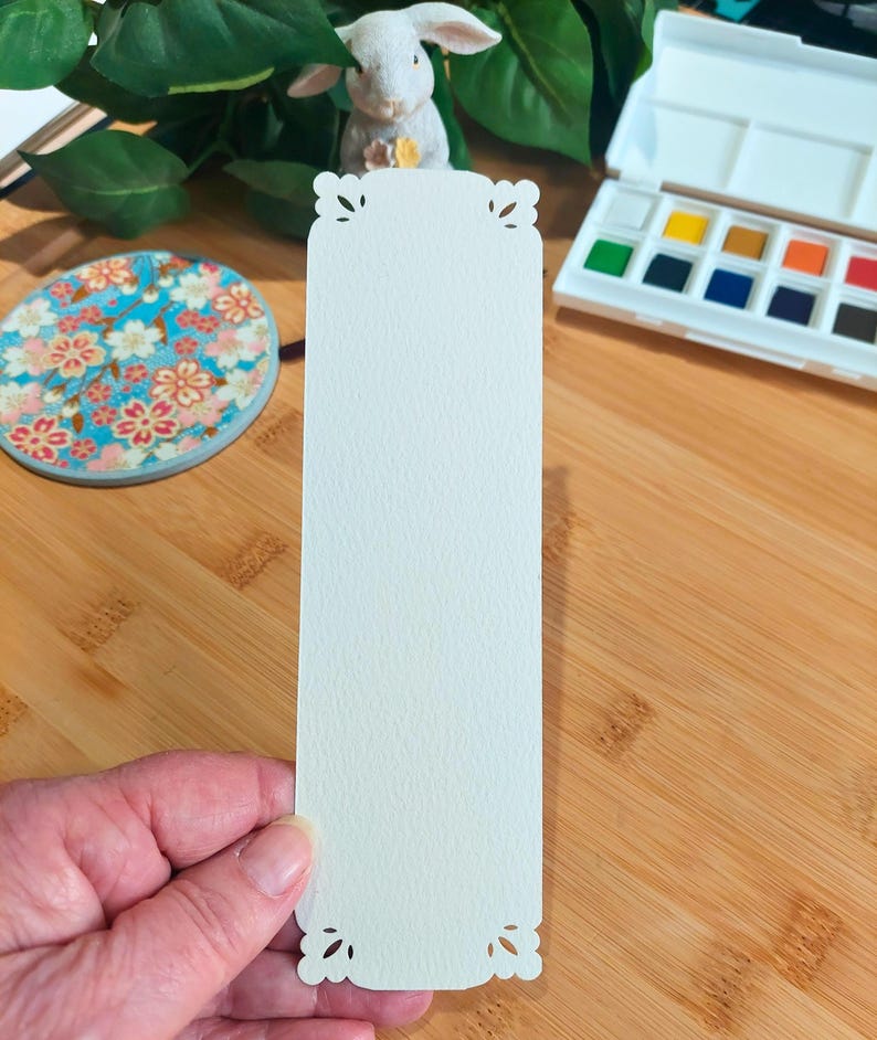 May include: A white bookmark with a decorative, scalloped edge. The bookmark is made of a textured paper and is blank.