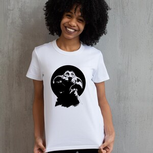 May include: A white short-sleeved t-shirt featuring a black graphic print of a house-elf character with large ears and wide eyes centered within a solid black circle on the chest. The design is presented as a digital file format listing SVG, PNG, EPS, and DXF.