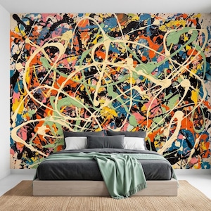 Könnte beinhalten: Ein Bett mit einem dunkelgrauen Polsterrahmen, weißen Kissen und einer hellgrünen Tagesdecke vor einer Wand mit Tapete, die ein chaotisches, mehrfarbiges Farbspritzmuster in Schwarz, Orange, Blau, Gelb und Creme aufweist.