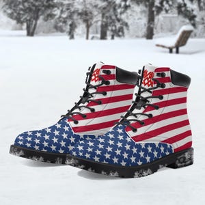 May include: A pair of combat boots with a patriotic design. The boots feature the American flag, with red and white stripes and blue star-covered panels. The boots have black laces and soles, and the text "SAVAGE" is printed on the top.
