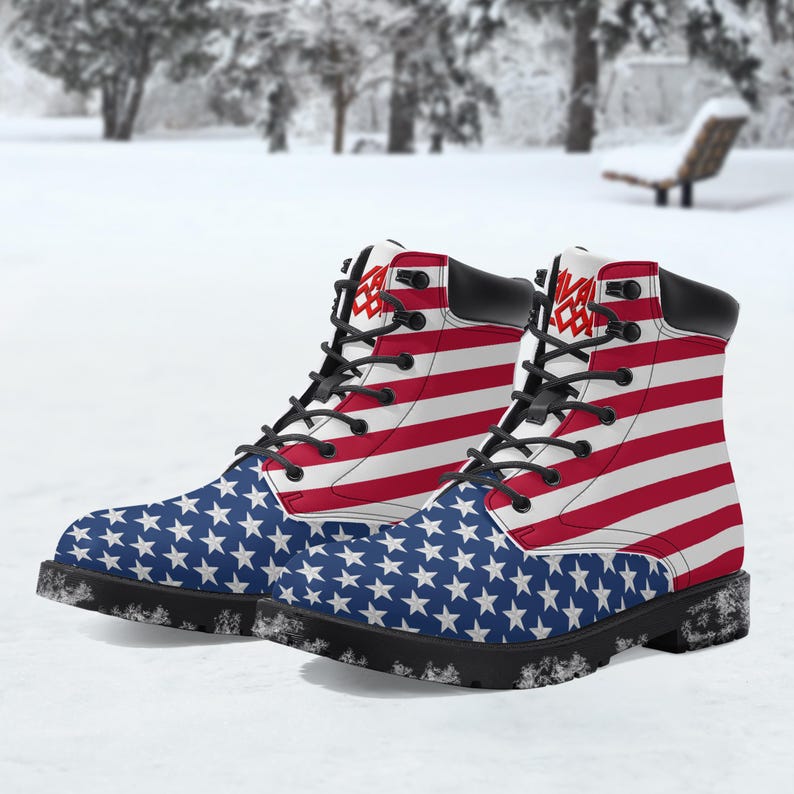 May include: A pair of combat boots with a patriotic design. The boots feature the American flag, with red and white stripes and blue star-covered panels. The boots have black laces and soles, and the text "SAVAGE" is printed on the top.