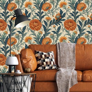 Op de afbeelding: Een woonkamer met een bruine leren bank, kussens en een deken. Het behang heeft oranje en blauwe bloempatronen. Een zwarte lamp en een bijzettafel staan op de voorgrond en creëren een gezellige sfeer.