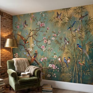 Op de afbeelding: Een gedetailleerde muurschildering met vogels, bloemen en bamboe tegen een teal en gouden achtergrond. Het kunstwerk bevat een verscheidenheid aan kleurrijke vogels die op takken met roze bloesems zitten. Een groene fauteuil en lamp staan op de voorgrond.