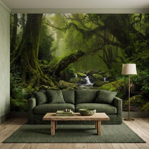 Op de afbeelding: Een muurschildering met bosthema met grote bemoste bomen en een beekje dat over rotsen stroomt. Voor de muur staat een donkergroene bank met vier kussens, een houten salontafel met boeken en een schaal, en een vloerlamp met een beige kap.