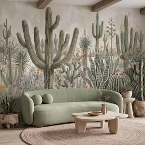 Pode incluir: Um sofá curvo verde-sálvia assenta sobre um tapete redondo tecido em frente a um mural de parede com vários cactos e plantas do deserto em tons verdes e terrosos. Uma mesa de centro de madeira clara com um pequeno vaso está à frente do sofá.