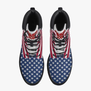 May include: Pair of black-soled boots featuring a patriotic design. The upper part of the boots displays the American flag with red and white stripes, while the lower part showcases a blue field with white stars. The boots have black laces and a black collar.
