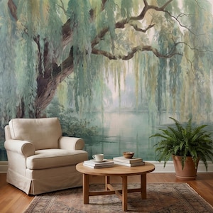 Könnte beinhalten: Ein ruhiges Interieur mit einem Wandbild einer Trauerweide über einem See. Ein beiger Sessel, ein runder Holztisch mit Büchern und einer Tasse sowie ein Topffarn vervollständigen die Szene.