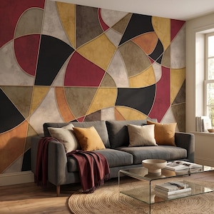 Può includere: Un soggiorno moderno con un divano grigio, cuscini e una coperta bordeaux. La parete presenta un grande design geometrico astratto nei toni del rosso, nero, oro e marrone. Un tavolino in vetro e un tappeto rotondo completano l'ambiente.