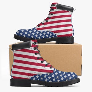 May include: Pair of combat boots featuring the American flag design. The boots have a red and white striped pattern on the upper part and a blue field with white stars on the toe. They have black soles, laces, and a black padded collar.