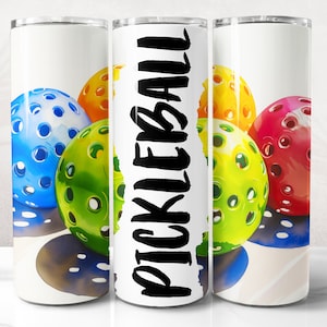 K&ouml;nnte beinhalten: Ein wei&szlig;er Becher mit einem bunten Bild von Pickleball-B&auml;llen und dem Wort "PICKLEBALL" in schwarzen Buchstaben.