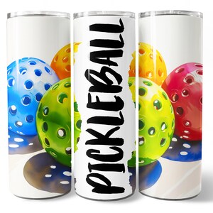K&ouml;nnte beinhalten: Ein wei&szlig;er Becher mit einem bunten Bild von Pickleball-B&auml;llen. Der Text "PICKLEBALL" ist in Schwarz auf dem Becher geschrieben.