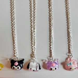 Puede incluir: Seis cadenas de plata con diferentes dijes de personajes. Los dijes son amarillos, blanco y negro, blanco, morado, rosa y blanco. Los dijes son todos personajes de dibujos animados con ojos grandes.
