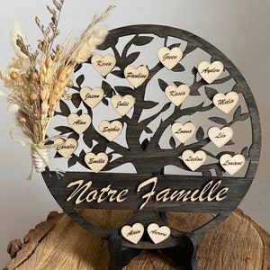 Peut inclure: Un arbre généalogique en bois avec des étiquettes de nom en forme de cœur. L'arbre est brun et a un pied noir. Les noms sur les étiquettes sont : Gwen, Kevin, Ayden, Pauline, Kasia, Melio, Jason, Julie, Alan, Sophie, Coralie, Emilie, Louna, Léo, Lelou, Louane, Alain et Antoine. L'arbre est décoré de fleurs séchées et de blé.