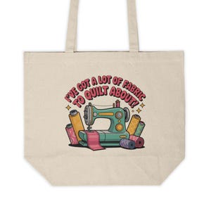 Puede incluir: Bolso tote beige con una ilustración colorida de una máquina de coser, carretes de hilo y el texto "I've got a lot of fabric to quilt about!". El bolso tiene forma rectangular y dos asas.