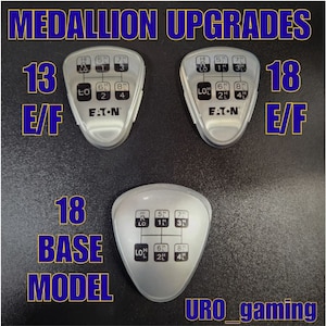 May include: Close-up of three silver gear shift knobs with black lettering. The knobs are labeled "13 E/F", "18 E/F", and "18 BASE MODEL". The knobs are labeled with gear numbers and "EATON".