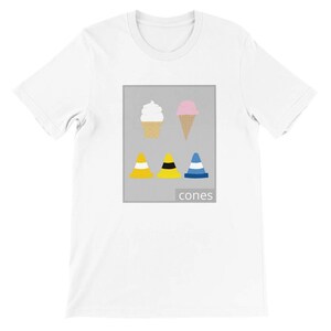 May include: White t-shirt featuring a graphic design with two ice cream cones and three traffic cones in yellow, black, and blue. The word "cones" is printed below the graphic.