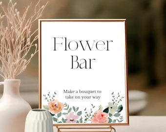以下が含まれることがあります： 「フラワーバー」と「Make a bouquet to take on your way」と書かれた、金色の縁取りのある白い看板。看板は、ピンク、ピーチ、グリーンの色合いの水彩画の花で飾られています。