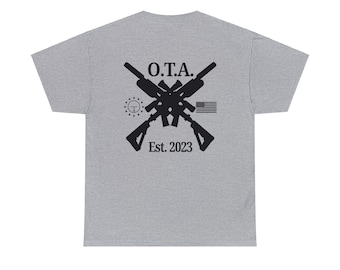 May include: A pale grey t-shirt with a black graphic on the back. The design includes crossed rifles, the letters "O.T.A.", a small American flag, and the text "Est. 2023".