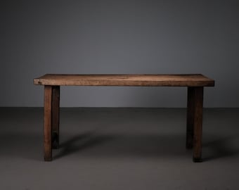 May include: A rustic wooden table with a simple design. The table has a rectangular top and four legs. The table is made of dark brown wood and has a natural finish.