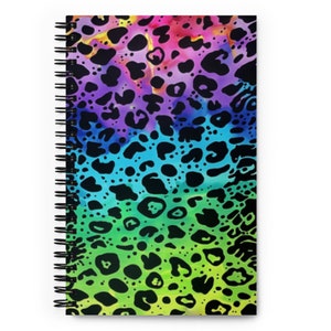 May include: A spiral-bound notebook with a vibrant, colorful cover. The cover features a rainbow gradient background with black leopard spots. The notebook's design is eye-catching and suitable for note-taking or journaling.