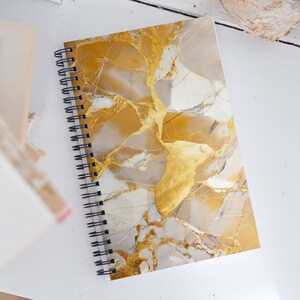 May include: A spiral bound notebook with a gold and white marble pattern cover.