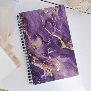 May include: Purple spiral bound notebook with a gold marble pattern.