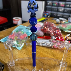 May include: A blue pen with a blue and green glitter ball on top. The pen is topped with a blue and black figurine of a cartoon dog with a grumpy expression.