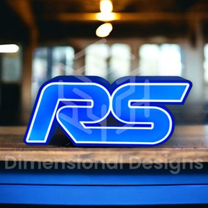 May include: A blue and white neon sign with the letters "RS" in a bold, stylized font. The sign is sitting on a wooden surface.