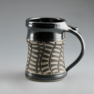 May include: A ceramic mug with a glossy black finish on the rim, base, and handle. The central body features a textured pattern of vertical, wavy black and white stripes. The mug has a sturdy, curved handle and a smooth, reflective surface throughout.