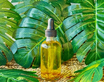May include: A clear glass bottle with a black dropper top filled with a yellow liquid. The bottle is sitting on a woven surface surrounded by green leaves.