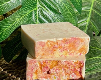 May include: Two bars of handmade soap with a pink and orange swirl pattern. The soap is sitting on a woven basket with green leaves in the background.