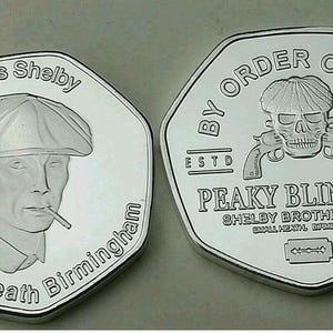 May include: Two silver coins featuring Peaky Blinders imagery. One coin depicts Thomas Shelby with text reading "Thomas Shelby Small Heath Birmingham". The other coin shows a skull with guns and the text "By Order of the Peaky Blinders".
