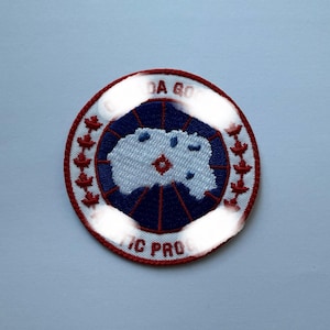 May include: Circular embroidered patch with a white and blue design, surrounded by a red border and red floral accents. The text "DA GO" and "TIC PRO" are visible on the patch.